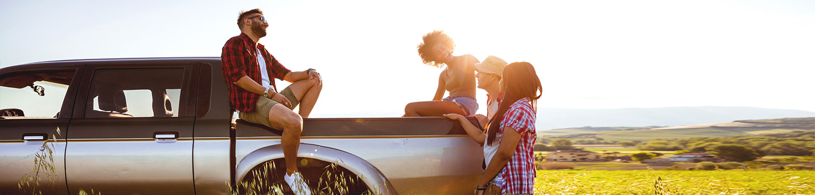 A group of young adults stand around a ute in a field