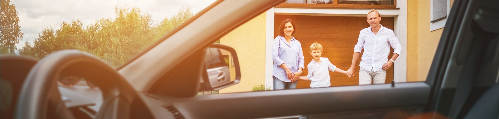man woman and boy standing in front of a garage door next to a parked car