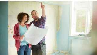 Couple standing in room undergoing renovation and holding plans