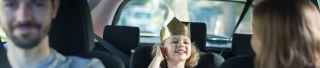 Girl wearing paper crown in back seat of car