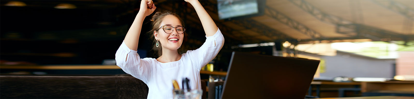 Happy woman celebrating success with arms raised up in front of laptop
