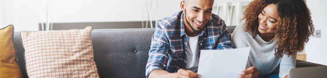 Couple smiling on the couch reading paperwork