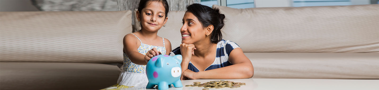 Mother looking at daughter putting money in blue piggy bank