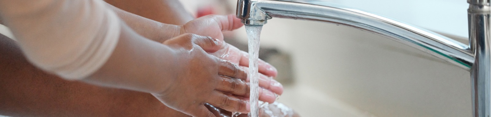An adult pair of hands and a child's pair of hands being washed under the same tap; 