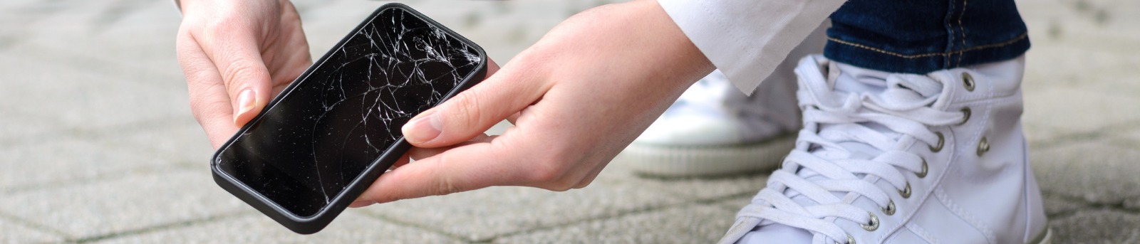 Close up of hands holding a phone with a cracked screen