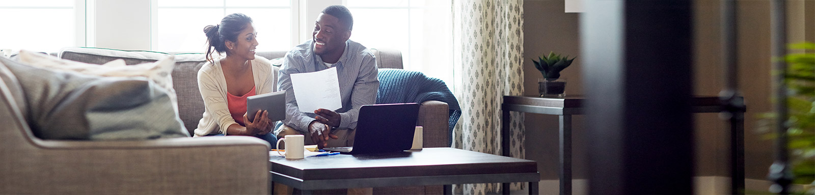 Couple on a sofa looking ath their ipad, papers, and laptop