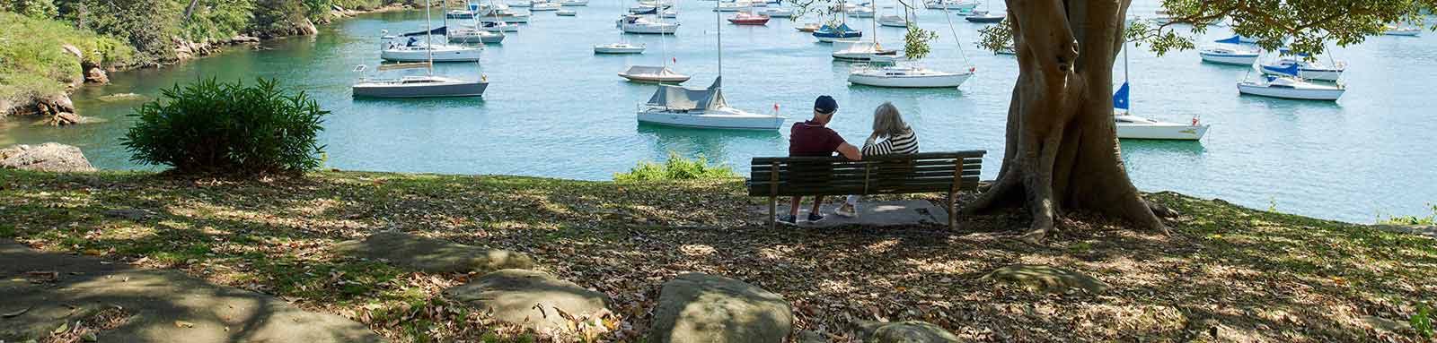 Elderly couple siting on a bench by the sea with boats
