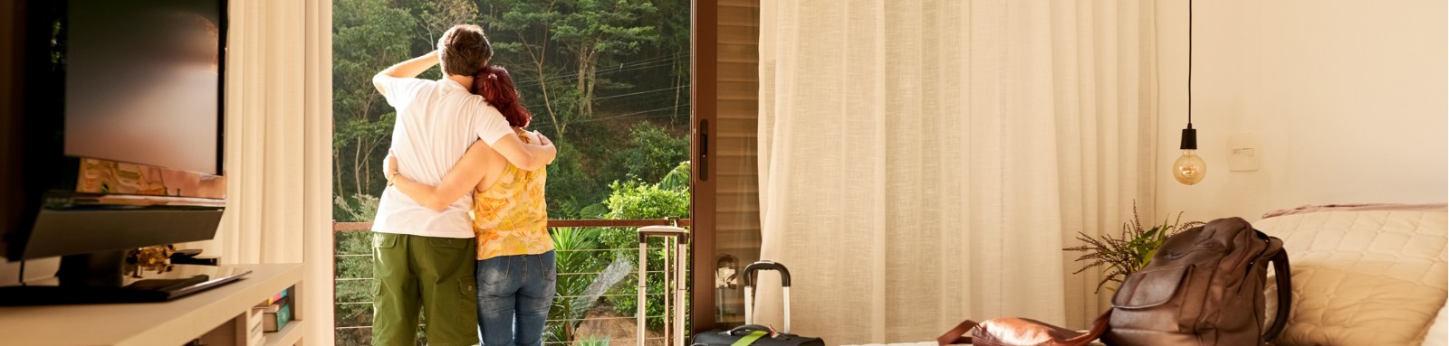 Man and woman embracing as they look at bush from bedroom