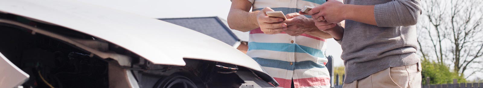 Two people standing at a wrecked car with mobile phones