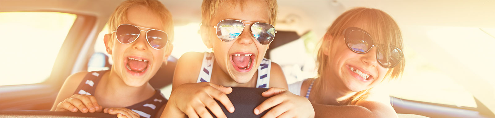 Kids in the backseat of car with sunglasses smiling