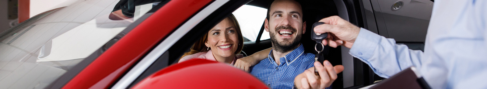 Couple in red car accepting car keys from salesman
