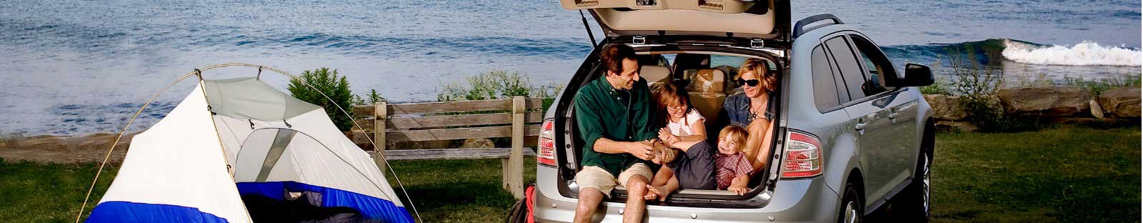 Family sitting in back of car next to beach tent