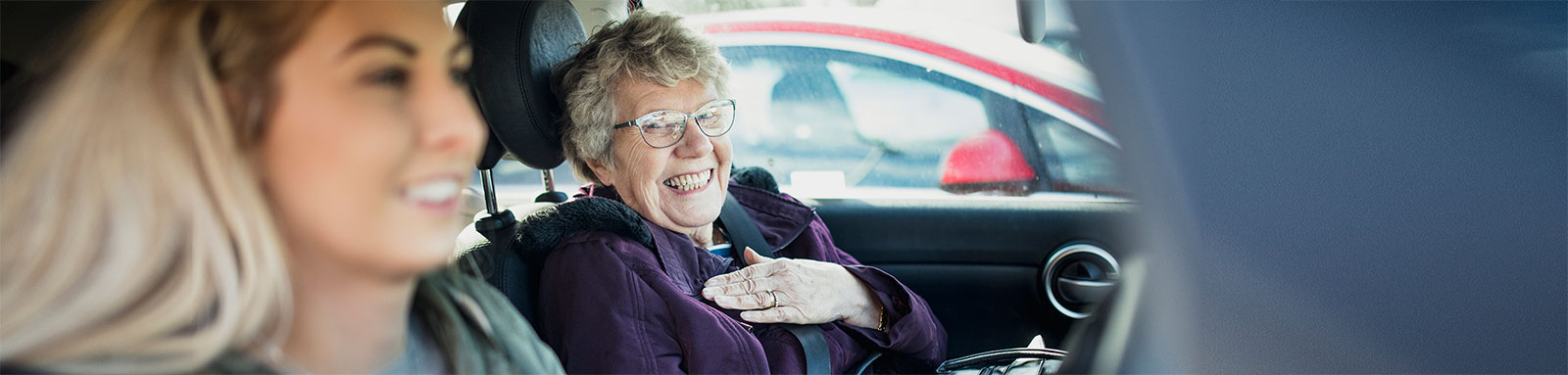 A blonde girl driving a car with grandma as passenger