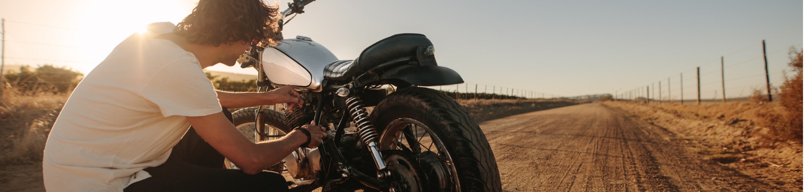 man checking his motorcycle on country road