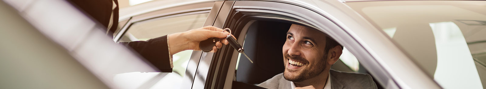 Man in a car smiling while a woman hands him a set of keys