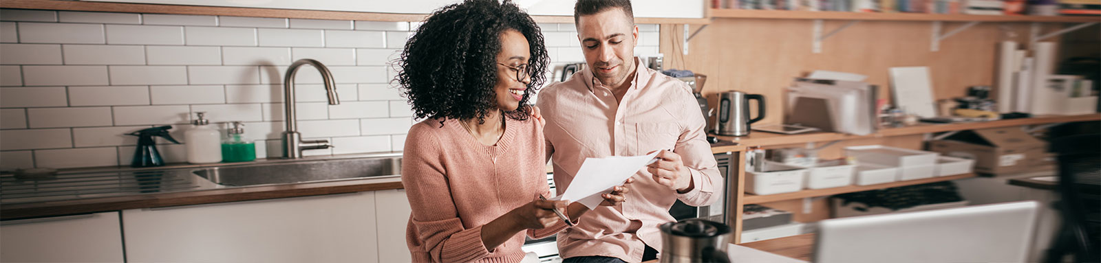 Couple discussing paper document in kitchen with coffee and laptop