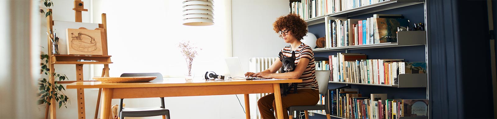 Woman on computer on a table with bookshelf behind her