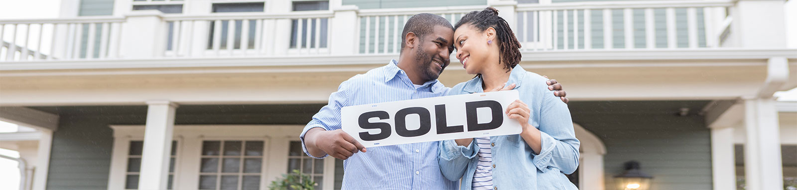 Couple holding sold sign in front of their home