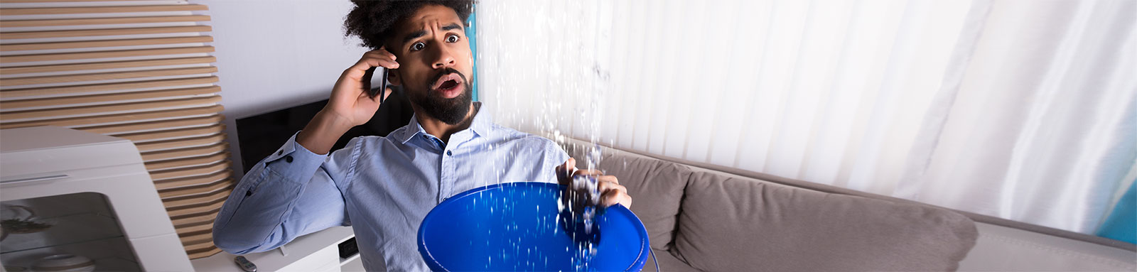 Man holding blue bucket under water leak in living room