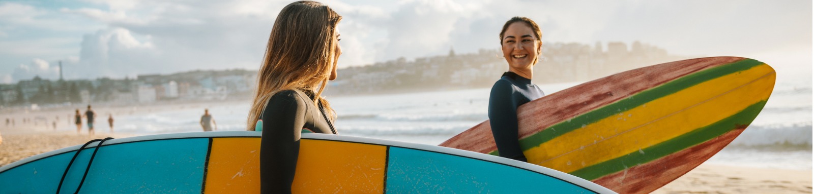 Two smiling women holding surfboards on the beach