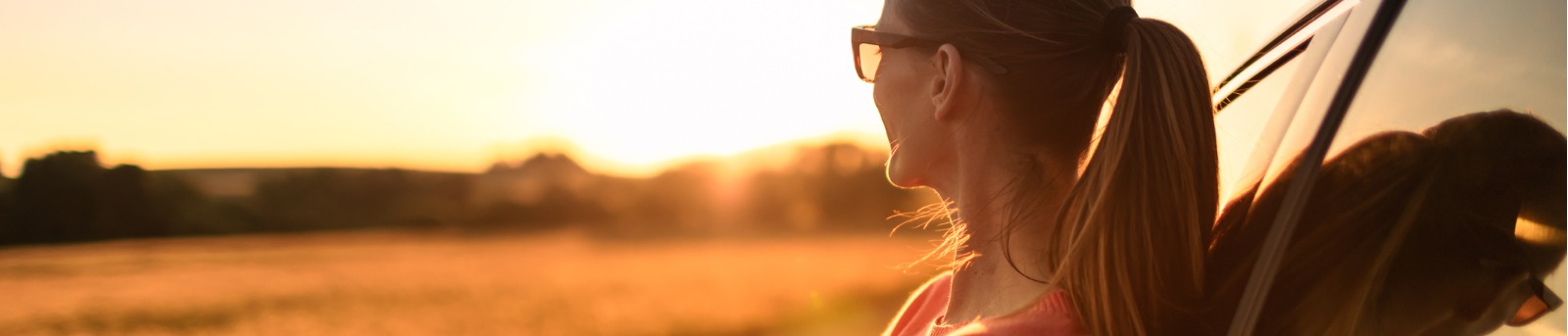 woman looking into the sunset next to car