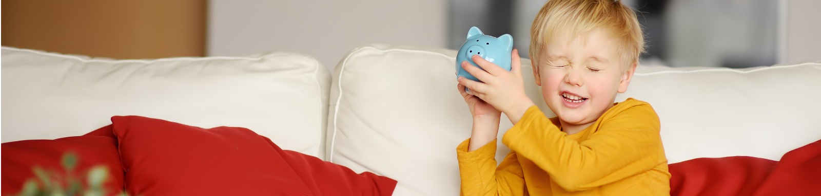 Little boy shaking blue piggybank on couch