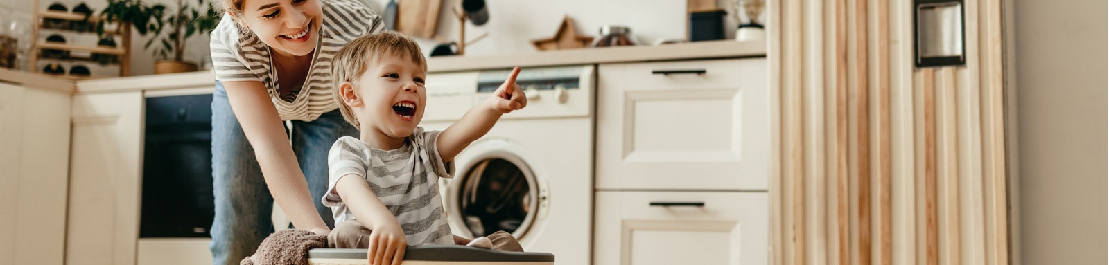 woman pushing child in laundry basket across floor