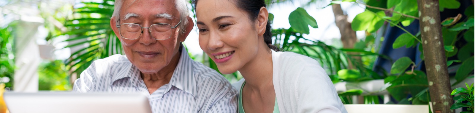 Elderly man and young woman looking at computer outdoors