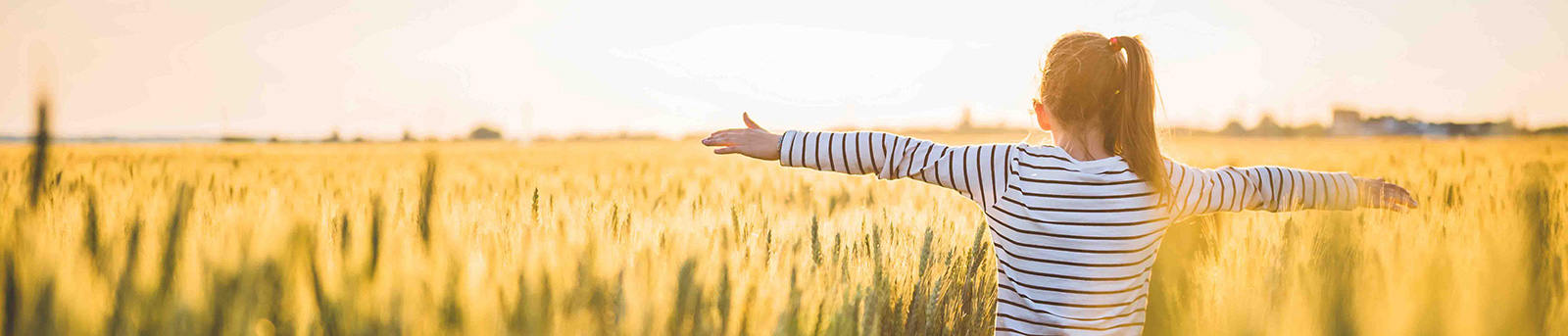 Girl in wheat field with arms stretched out