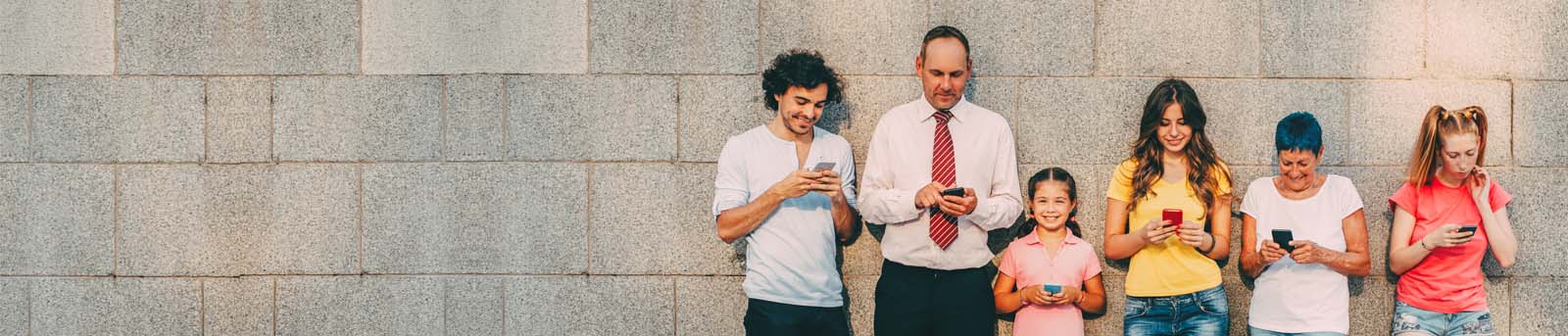 People standing against a brick wall holding mobile phones