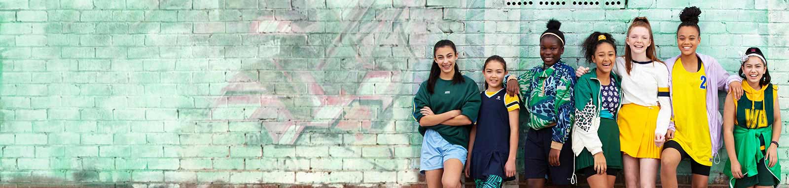 Netball girls standing infront of green brick wall