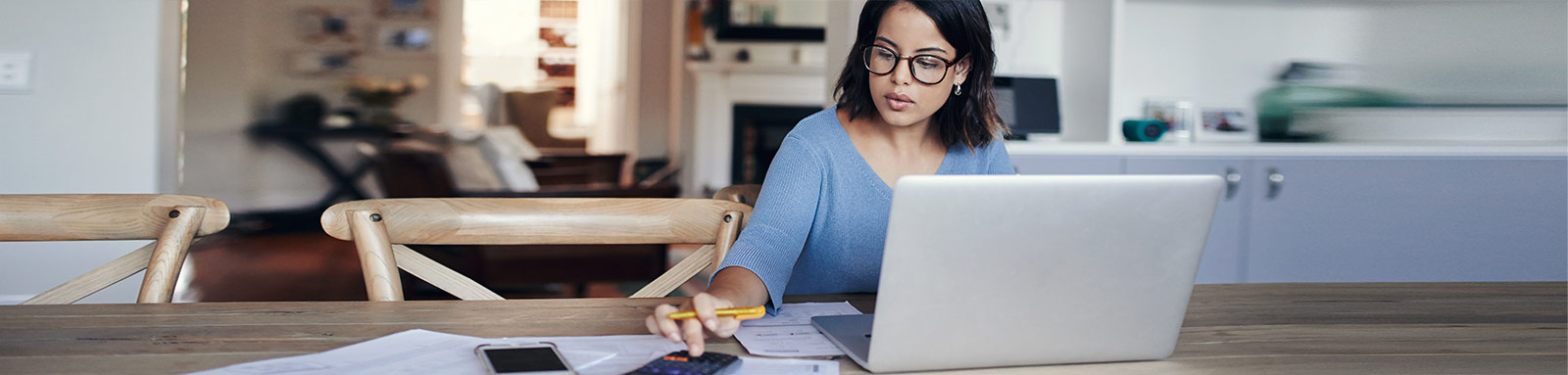 Woman working on dining table with laptop and calculator