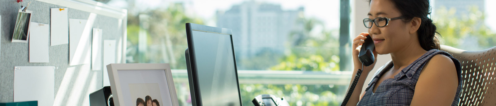 A woman at desk  with monitor & talking over mobile phone.