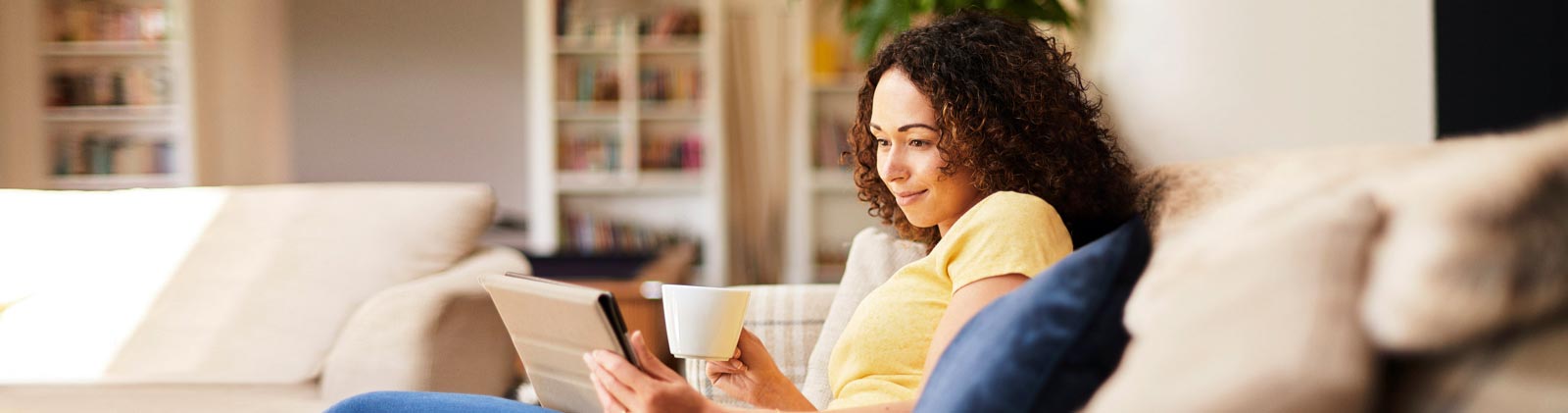 A woman on the couch with a mug and iPad