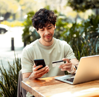 Man holding phone and credit card in front of laptop