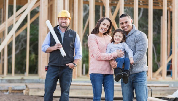 Family with builder standing in front of house frame