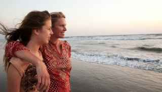 Mother and daughter smiling at the beach in the sun